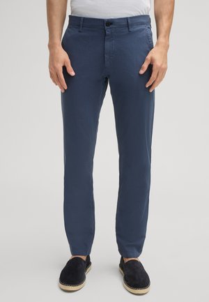 Marineblaue Chinos aus leichtem Stoff, mit schmaler Passform, Knopfverschluss und flacher Vorderseite, kombiniert mit schwarzen Slippers.