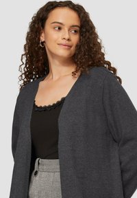 Ciemnoszary kardigan o luźnym fasonie, z dekoltem w serek. Pod spodem czarny top z falbaniastym koronkowym wykończeniem. Widoczna fakturowana tkanina.