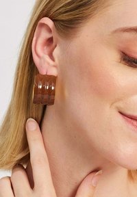 Bružas akrila riņķa auskari ar ribotām tekstūrām. Auskariem ir spīdīga apdare un apļa forma, izceļot to unikālo dizainu.