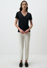 Czarny t-shirt z dekoltem w serek i krótkimi rękawami, w zestawieniu z białymi spodniami slim fit i czarnymi loafersami. Prosty design i gładka tekstura.