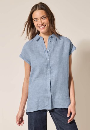 Helles blaues Leinenhemd mit kurzen Ärmeln, Knopfverschluss und Kragen. Unregelmäßiger Saum, glatte Textur und lässiges Design.