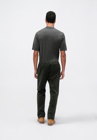 Koolgrijze t-shirt met korte mouwen gecombineerd met donkergroene corduroy broek, met een elastische tailleband en diepe zakken. Bruine suède schoenen.
