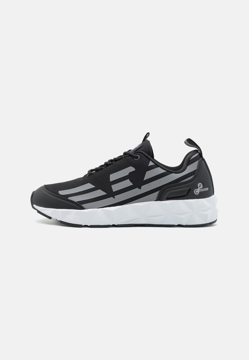 Black athletic shoe featuring a mesh upper with grey accents, a thick white geometric sole, and a pull tab at the heel for easy wear.