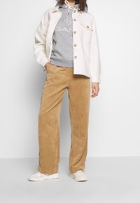 Pantalones de pana beige de pierna ancha, sudadera gris clara con logo y chaqueta exterior color blanco roto con botones y dos bolsillos delanteros. Calzado casual.