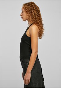 Svart ribbet topp med en tettsittende design. Sidesynet viser en høy halslinje og tynne stropper, kombinert med svarte denimjeans.