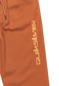Rostfarbene Jogginghose aus weichem Baumwollgemisch, mit einem bestickten Logo in leuchtendem Orange an der Seite. Elastischer Bund mit Kordelzug.
