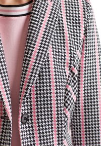 Marynarka w czarno-białą kratę houndstooth, akcentowana różowymi paskami. Posiada klapy z wycięciem, zapięcie na guziki oraz fakturowany materiał.