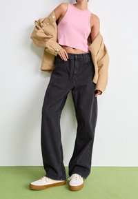 Roze geribbelde cropped tanktop, beige oversized jas, zwarte wijde jeans en crèmekleurige sneakers met bruine zolen op een groene vloer.