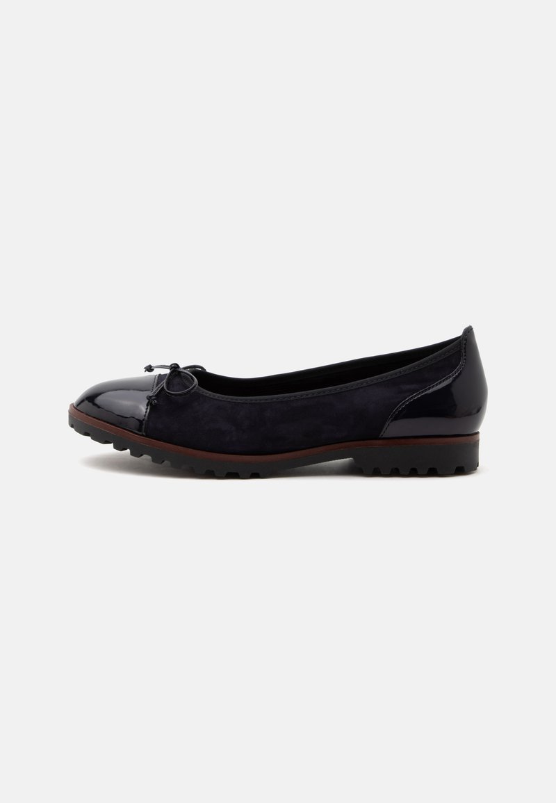 Chaussure plate noire avec un bout rond brillant, petit nœud à l'avant, côtés en daim et semelle rainurée sur fond blanc.