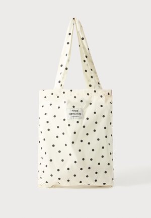 Kremowa torba typu tote w czarne kropki z długimi uchwytami, z białą etykietą z napisem "Mads Nørgaard Copenhagen".