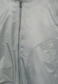 Grijze bomberjas met een gladde, glanzende textuur, een centrale ritssluiting en doorgestikte accenten op de zakken. Lichtgewicht, casual ontwerp.