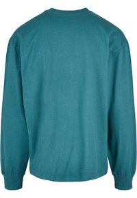 Hosszú ujjas, crewneck fazonú pulóver teal színű pamutból. Jellemzője a passzos mandzsetta, sima felület és az egyszerű, egyszínű dizájn, látható minták nélkül.