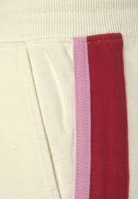 Crème-kleurige stof met verticale strepen in roze en rood. Lichtjes textuur met zichtbare naden en een zachte afwerking.