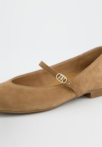 Hnědý semišový baletní střevíček s nízkým podpatkem, zaoblenou špičkou a zlatým přezkovým zdobením na pásku přes nárt.