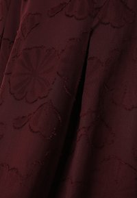Deep burgundy fabric with raised floral jacquard pattern and soft folds creating shadows and texture.