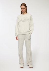Jasnoszary dres składający się z bluzy z okrągłym dekoltem z napisem "Stockholm Leisure Club" oraz dopasowanych spodni o szerokich nogawkach. Materiał z mieszanki bawełny.
