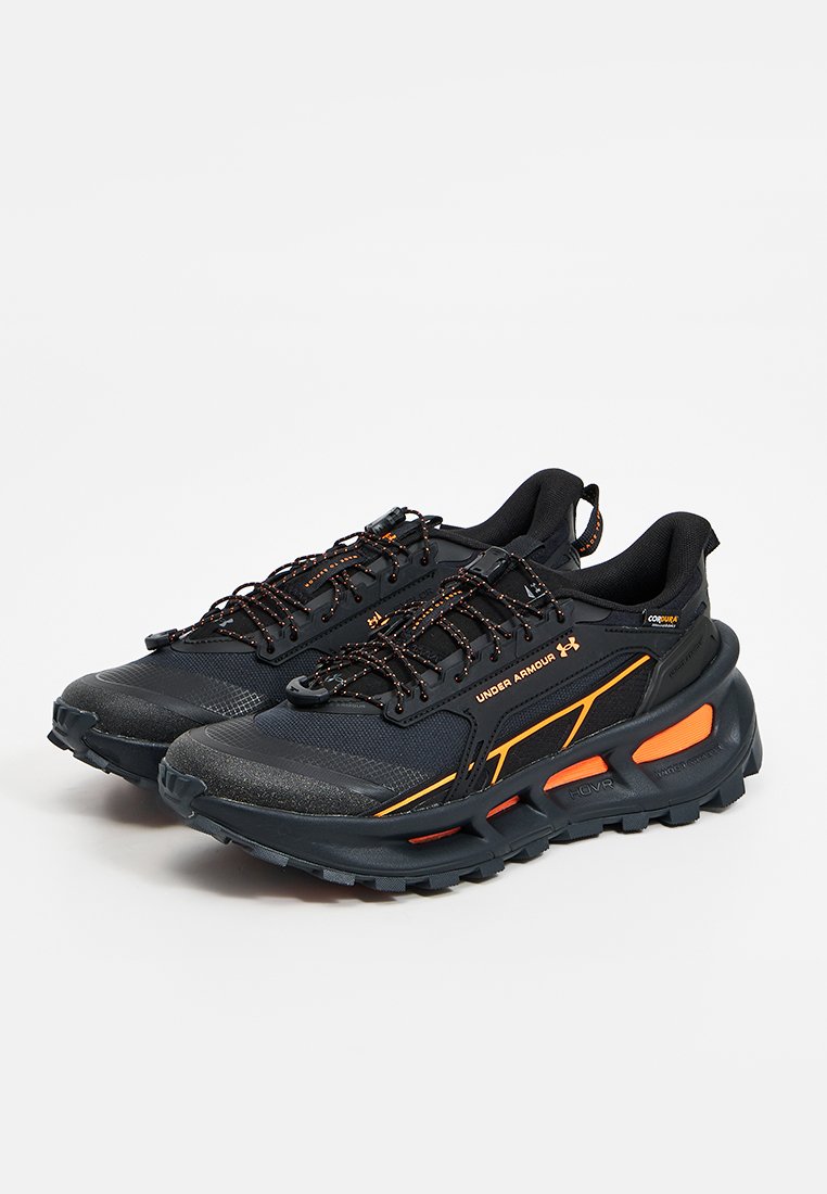 Par de zapatillas deportivas Under Armour negras con detalles en naranja, suelas resistentes y cordones negros con detalles reflectantes sobre un fondo blanco.