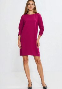 Sukienka w kolorze magenta typu shift, z rękawami za łokieć, gładką teksturą i rozcięciami po bokach. W zestawieniu z czarnymi szpilkami z zaostrzonymi noskami.