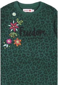 Zielona bluza z nadrukiem w panterkę, z kolorowym haftem kwiatowym i wyraźnym napisem "Wolność" w kolorze czarnym.