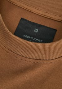 Brown cotton t-shirt with a ribbed crew neck. Features a black label with "JACK & JONES" logo. Smooth texture and even stitching.
