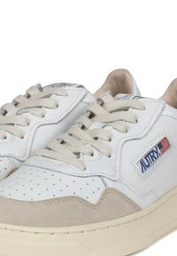 Sneaker bianche in pelle con dettagli in suede beige, punta perforata, lacci crema e branding sul lato con dettagli rossi e blu.