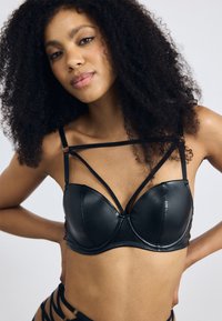 Reggiseno in pelle nera con coppe sagomate, dettagli a tracola incrociata e texture liscia. Le tracolle hanno accenti dorati per un ulteriore dettaglio di design.