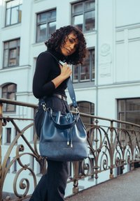 Kék bőrből készült vödör táska sima és texturált felületekkel, húzózsinóros záródással és arany színű kiegészítőkkel.