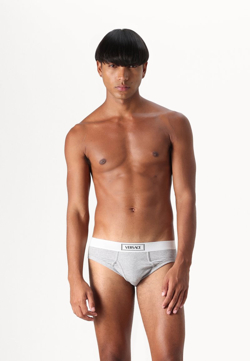 Grijze katoenen slips met een witte elastische tailleband waarop het "VERSACE"-logo staat, met een aansluitend ontwerp en een subtiele textuur.