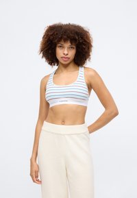 Ανοιχτό μπλε ριγέ αθλητικό bralette με λευκή ελαστική ταινία που φέρει το λογότυπο "Calvin Klein". Το υλικό φαίνεται ελαστικό, σχεδιασμένο για άνεση.