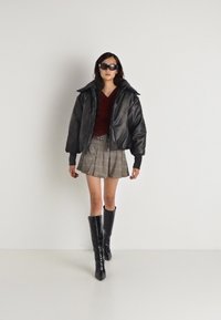 Jackett din piele neagră, bluză vișinie, fustă mini în carouri, cizme negre până la genunchi și ochelari de soare completează look-ul. Texturi netede și forme structurate.