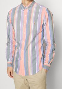 Randig skjorta med knappar i flera färger som har pastellfärgade rosa, lila, grå och blå ränder. Tillverkad av lätt tyg med en klassisk krage.