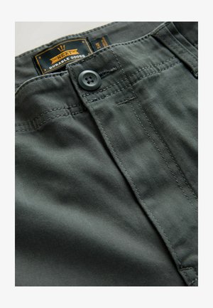 Grå stofbukser med knaplukning. De har synlige stikningsdetaljer og et sort indre mærke med brandnavnet.