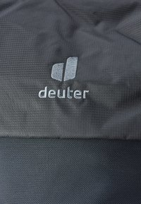 Must mustkott, millel on tekstureeritud pind. Omab õmmeldud halli logo "deuter" ning selle kohal on kaks abstraktset kuju.