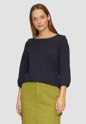 Navyblauwe, lange mouwen top met een ronde halslijn, met verzamelde mouwen. Gecombineerd met een groene rok tot de knie met zakken.