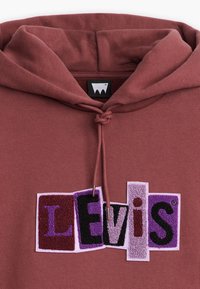 Mauve mikina s texturovanými nášivkami písmen "Levi's" v purpurové, černé a vínové barvě na přední straně, kapuce se šňůrkou svázanou do uzlu.