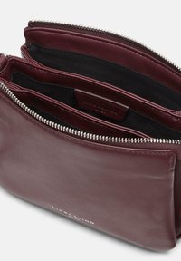 Bordowa skórzana saszetka na zamek z dwiema głównymi komorami, czarne wnętrze z tkaniny oraz białe logo "Liebeskind Berlin" na froncie.