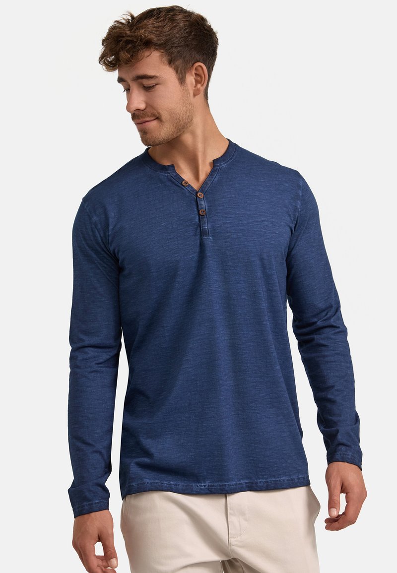 Langärmliges, marineblaues Henley-Shirt aus weichem Stoff mit strukturierter Oberfläche, das drei Holzknöpfe am Kragen und einen abgerundeten Saum aufweist.