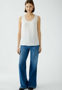 Haut sans manches blanc en tissu lisse, associé à un jean évasé bleu. La tenue présente un design simple sans motifs visibles.