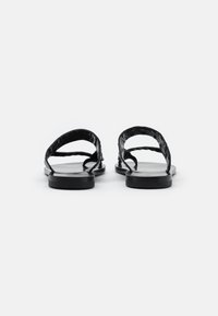 Sandales plates noires avec une semelle lisse, un design minimaliste et des lanières texturées avec un détail tordu, vues de l'arrière.