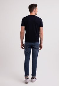 Námořnické tričko s krátkým rukávem vyrobené z měkké látky, v kombinaci s úzkými modrými džíny a bílými teniskami s černými akcenty. Jednoduchý design.