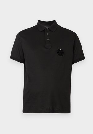 Zwart poloshirt van katoen. Voorzien van een drieknopenlijst, korte mouwen en een ronde logopatch op de linkerborst.