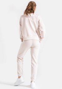 Jasnoróżowa bluza z kapturem i dopasowane spodnie wykonane z miękkiego materiału, cechujące się luźnym krojem i ściągaczami, zestawione z białymi sneakersami.