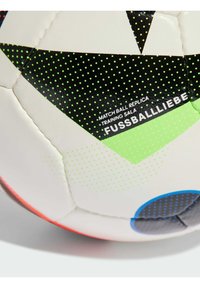 Biała piłka nożna z czarnymi i zielonymi wzorami geometrycznymi, charakteryzująca się gładką syntetyczną powierzchnią i kropeczkami zapewniającymi chwyt. Tekst zawiera "REPLIKA PIŁKI MECZOWEJ."