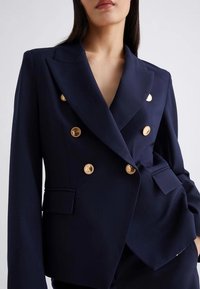 Blazer doppiopetto navy con bottoni dorati, rever a notched e due tasche frontali. Realizzato in tessuto strutturato con vestibilità tailored.