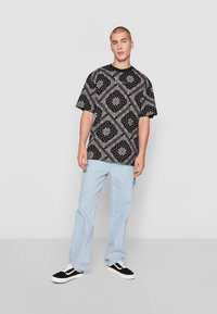 T-shirt oversize a righe bianche e nere con maniche corte, abbinato a jeans dritti blu chiaro e sneakers nere.