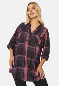 Camicia a quadri nei toni del nero, viola e rosa; vestibilità comoda con scollo a V, maniche arrotolate e taschino sul petto; tessuto testurizzato.