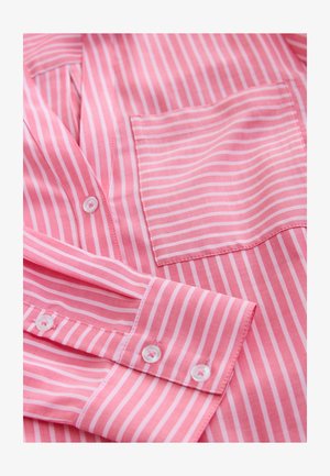 Rózsaszín-fehér csíkozású ing. Könnyű anyagból készült, mellkasi zsebbel. Gombok díszítik a gombsor mentén és az ujjatlan mandzsettán.