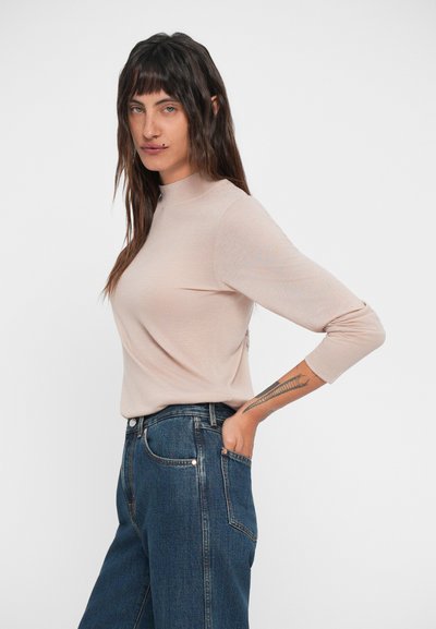 Camiseta de manga larga beige clara con cuello alto, combinada con jeans azul oscuro. La camiseta tiene una textura suave y un ajuste relajado.