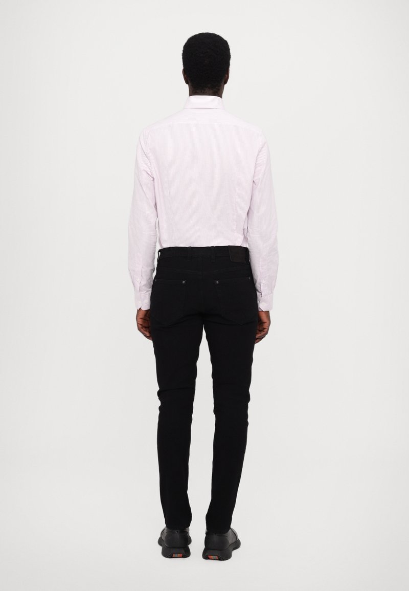 Hellrosa gestreiftes Langarmhemd mit Button-down-Kragen, kombiniert mit schwarzen Slim-Fit-Jeans und schwarzen Schuhen, von hinten betrachtet.