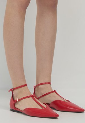 Rote flache Schuhe mit einer spitzen Zehenform, aus glattem Leder gefertigt. Sie verfügen über Knöchelriemen und ein niedriges Profil mit einem eleganten, minimalistischen Design.
